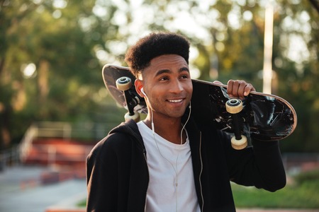 Young happy skateboarder man holding skateboard on his shoulders at public parkの写真素材