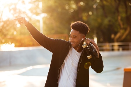 Portrait of a male teenager guy holding skateboard on shoulders and looking at sunset outdoorsの写真素材
