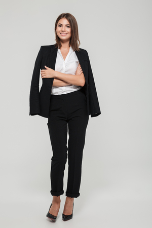 Full length portrait of a happy pretty woman in suit with jacket on her shoulders standing and looking at camera isolated over white backgroundの写真素材
