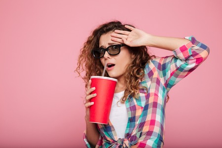 Young frightned caucasian woman in 3d glasses with cola afraid of film isolated over pinkの写真素材