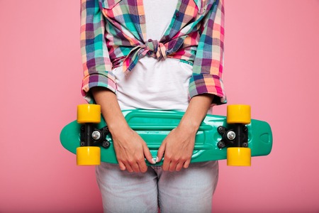 Smiling pretty brunette lady in shirt hugging her green skateboard and posing isolatedの写真素材