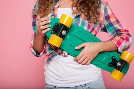Smiling pretty brunette lady in shirt hugging her green skateboard and posing isolatedの写真素材