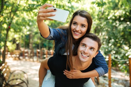 Portrait of a young happy couple in love making selfie at the park, piggyback rideの写真素材