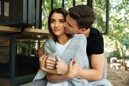 Portrait of a sensual young couple embracing while sitting in a cafe outdoorsの写真素材