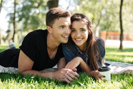 Portrait of happy couple drinking coffee while laying on a blanket together and laughing outdoorsの写真素材