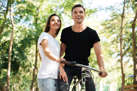 Portrait of a young smiling couple riding on a bicycle together at a parkの写真素材