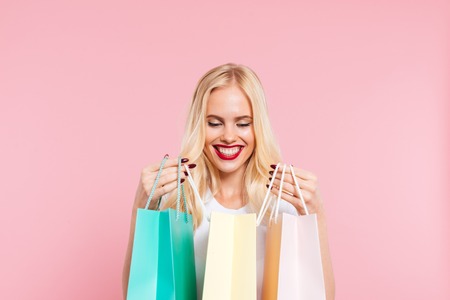 Image of Pleased blonde woman looking at packages over pink backgroundの写真素材
