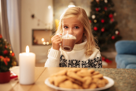 Beautiful blonde girl drinking cacao with marshmallow, looking at camera on Christmas breakfastの写真素材