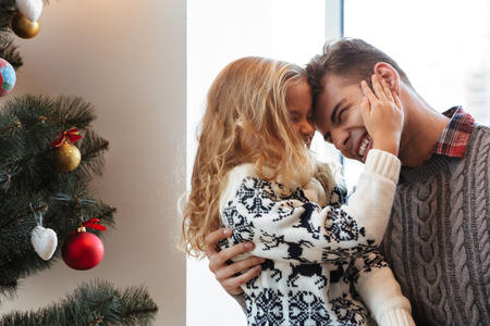 Cute blonde girl touching fathers face with closed eyes near Christmas treeの写真素材
