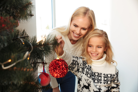Happy little girl decorating christmas tree with her mother at homeの写真素材