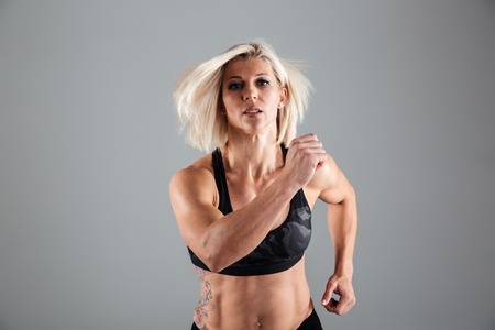 Portrait of a motivated adult female athlete running towards camera isolated over gray backgroundの写真素材