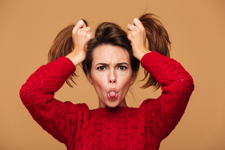 Picture of funny caucasian woman dressed in sweater standing isolated. Looking camera showing tongue.の写真素材