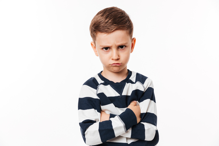 Portrait of an upset cute little kid standing with arms folded and looking at camera isolated over white backgroundの写真素材