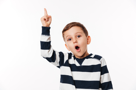 Portrait of an excited smart little kid pointing finger up and looking at camera isolated over white backgroundの写真素材