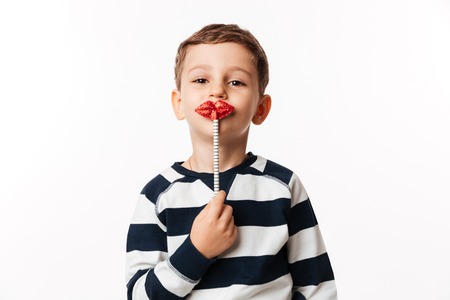 Portrait of a funny cute little kid holding paper lips on a stick and looking at camera isolated over white backgroundの写真素材