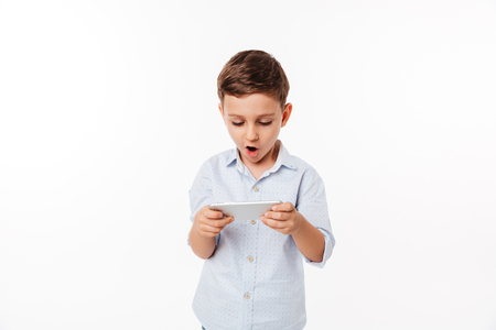 Portrait of an amused cute little kid playing games on smartphone isolated over white backgroundの写真素材