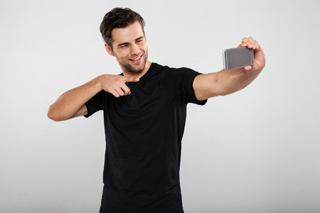 Image of young sportsman isolated over grey wall background. Looking aside make selfie by mobile phone pointing.の写真素材