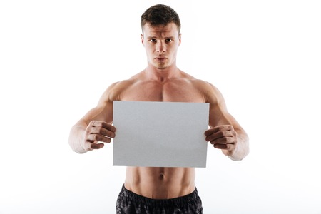 Image of serious handsome young sportsman standing isolated over white background and holding copyspace paper. Looking camera.の写真素材