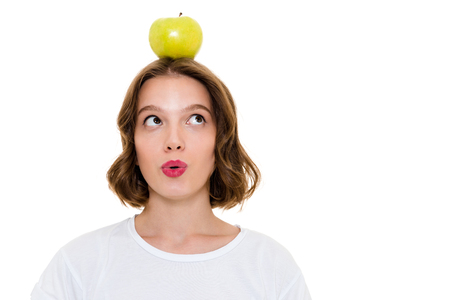 Image of thinking pretty caucasian woman holding apple on head standing isolated. Looking aside.の写真素材