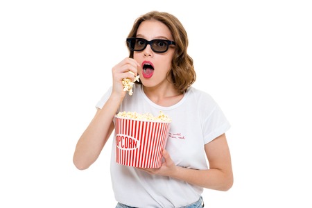 Image of concentrated caucasian woman holding pop corn wearing 3d glasses standing isolated. Looking camera watch film.の写真素材