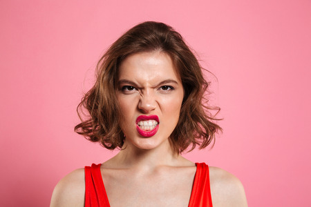 Close-up portrait of angry young woman with red lips looking at camera, isolated on pink backgroundの写真素材
