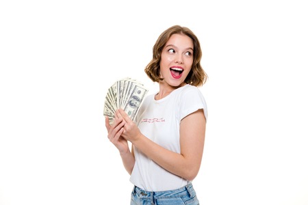 Close up portrait of a joyful young girl holding bunch of money banknotes and looking away at copy...