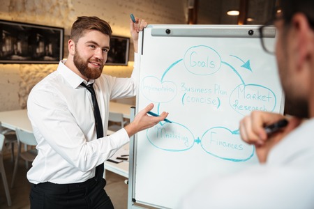 Two smart businessmen having a meeting and discussing business plan on a blackboard indoors