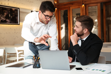 Businessmen discuss corporate goals in front of laptops at workplace in officeの写真素材