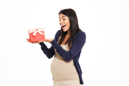 Portait of a cheerful happy pregnant woman holding gift box isolated over white backgroundの写真素材