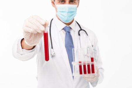 Cropped image of a serious young male doctor with stethoscope dressed in uniform holding ampoules isolated over white backgroundの写真素材