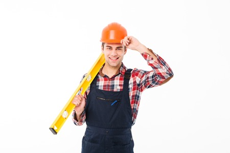 Full length portrait of a happy young male builder holding spirit level tool while standing and...