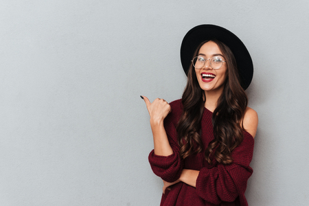 Young beautiful hipster girl showing thumb up gesture, looking at camera, isolated on gray backgroundの写真素材