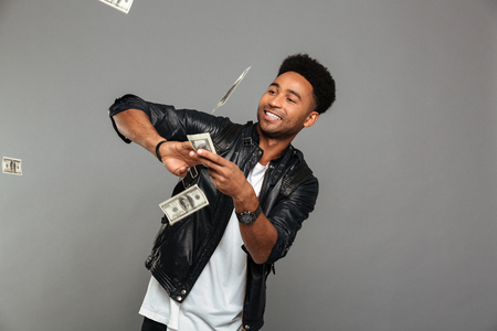 Funny afro american rich man scattering dollars banknotes, isolated over gray backgroundの写真素材