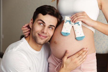 Cropped photo of cheerful man hug belly of his lovely pregnant wife indoors at home and try to hear...