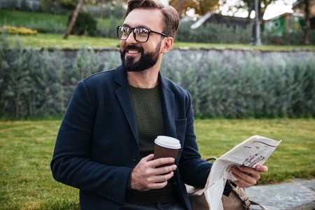 Portrait of a smiling young man sitting with a newspaper and holding coffee cup outsideの写真素材