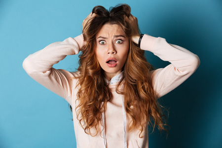 Photo of displeased shocked young woman standing isolated over blue wall background. Looking camera.の写真素材