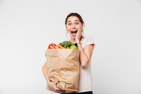 Portrait of a happy excited girl holding bag with groceries and screaming isolated over white backgroundの写真素材