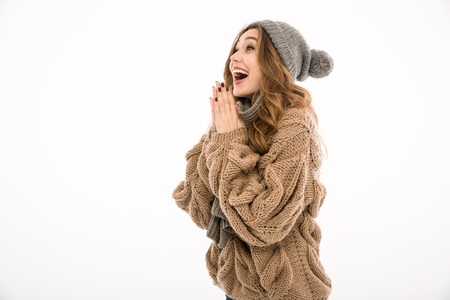 Excited surprised young cute woman dressed in warm sweater and scarf standing isolated over white wall background. Looking aside.の写真素材