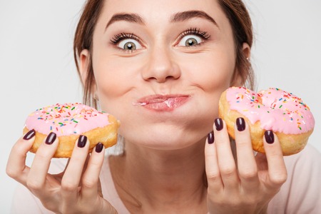 Close up portrait of a satisfied pretty girl eating donuts isolated over white backgroundの写真素材