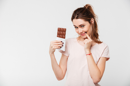 Portrait of a lovely pretty girl holding chocolate bar and looking at camera isolated over white backgroundの写真素材
