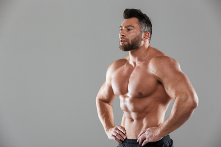 Portrait of a healthy strong shirtless male bodybuilder standing and looking away isolated over gray backgroundの写真素材