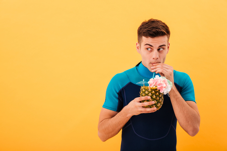 Picture of Pensive mystery surfer in wetsuit drinking cocktail and looking away over yellow backgroundの写真素材