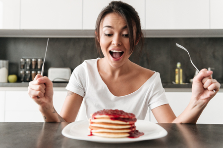 Picture of hungry young woman sitting at the kitchen in home. Looking at pancakes.の写真素材