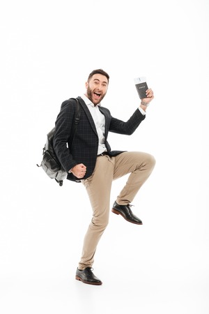 Full length portrait of a joyful excited man holding passport with flying tickets and celebrating isolated over white backgroundの写真素材