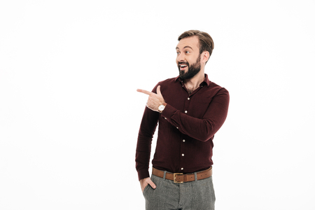 Portrait of an excited bearded man standing and pointing finger away isolated over white backgroundの写真素材