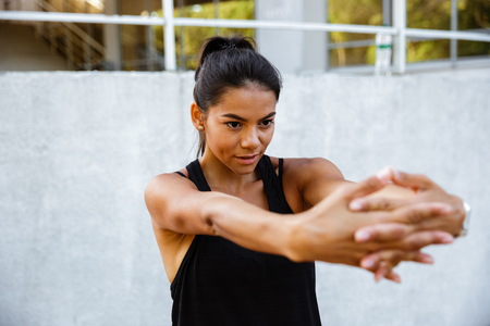 Portrait of a concentrated fitness girl stretching her hands while standing outdoorsの写真素材