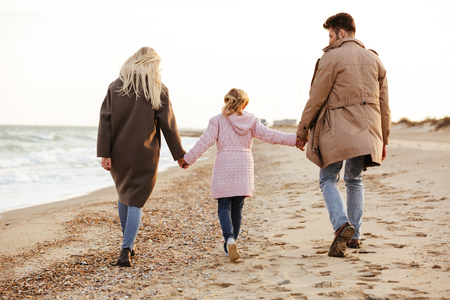Back view of a young family with a little daughter walking along the beach together holding handsの写真素材