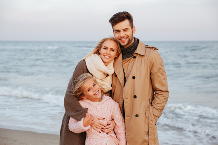 Portrait of a smiling family with a little daughter standing the beach together and huggingの写真素材