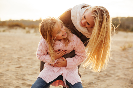 Beautiful mother playing with her little daughter at the beachの写真素材