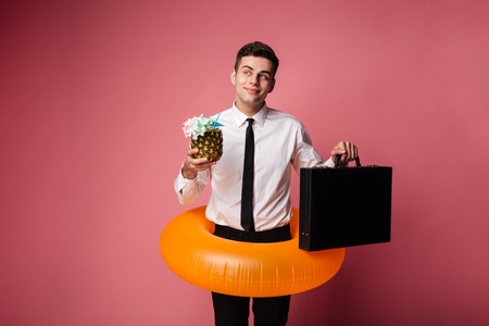 Young businessman in swimming circle holding brief-case and cocktail and dreaming about rest isolatedの写真素材